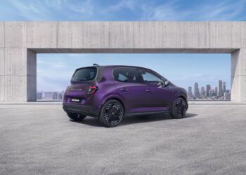 Three-quarter rear view of a purple Nissan PIXO electric city car parked beneath a modern concrete structure, with a city skyline in the background.